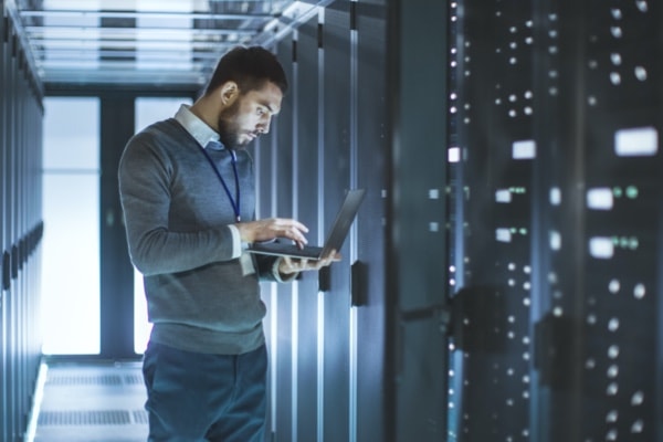 Man holding laptop by row of server cabinets